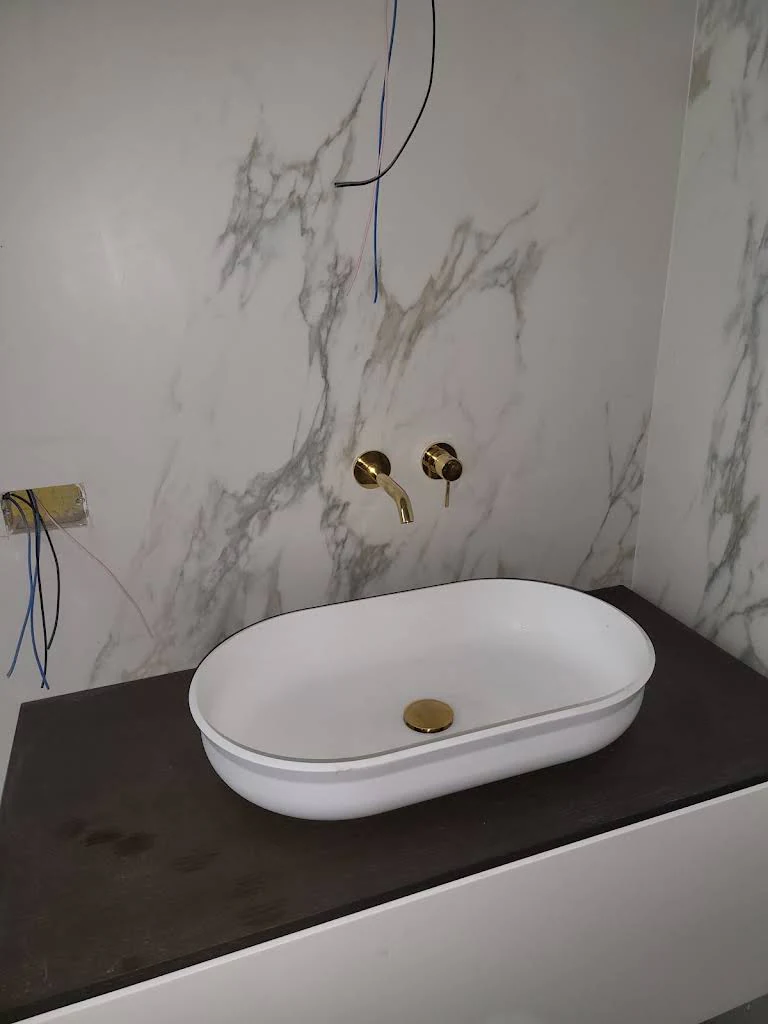 Lavabo bianco su piano scuro e parete chiara venata